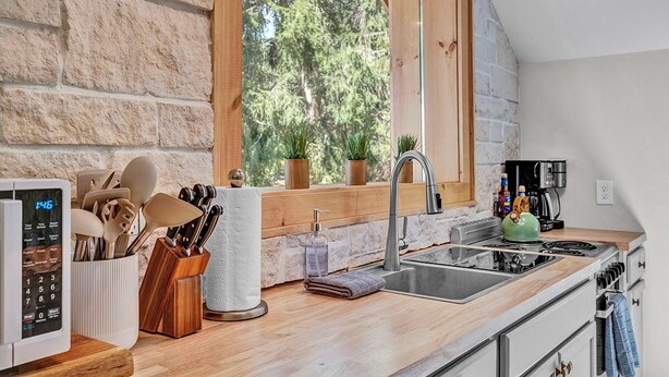 A modern kitchen with a stone wall, wooden countertop, and a window with a view of trees.