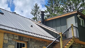 A stone house with a metal roof, wooden staircase, and a small porch.