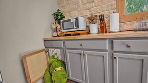 A kitchen with a microwave, wooden countertop, cabinets, and a green plush toy.