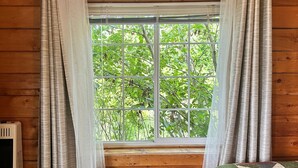 Una habitación con paredes de madera, una ventana que da a árboles verdes y un radiador a la izquierda.