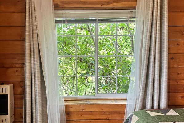 Una habitación con paredes de madera, una ventana que da a árboles verdes y un radiador a la izquierda.