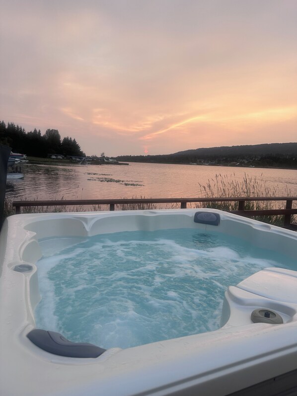 A hot tub with a view of a lake and hills during sunset.