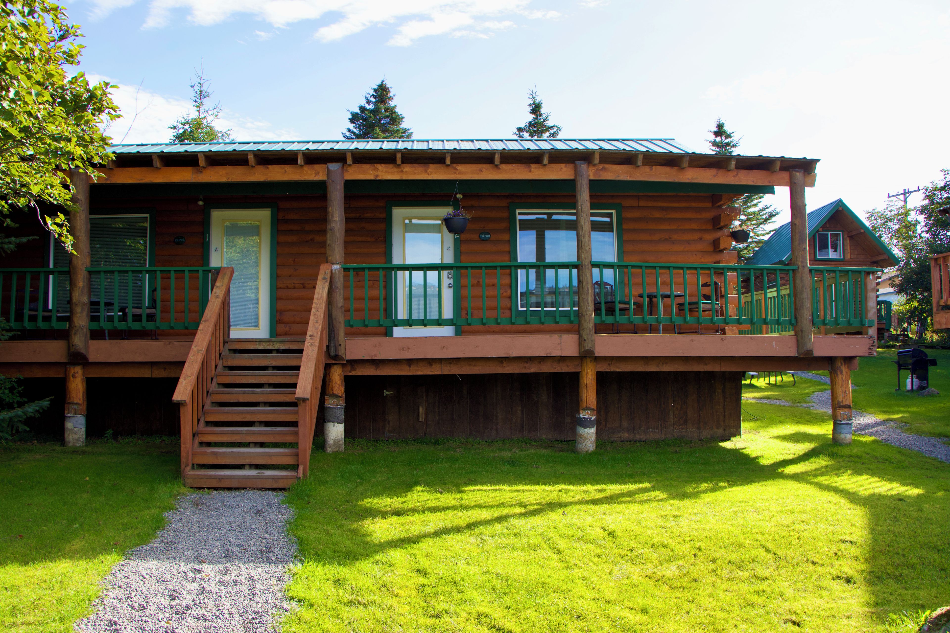 Eine Holzhütte mit überdachter Veranda, einer Treppe zum Eingang und einem Kiesweg davor.