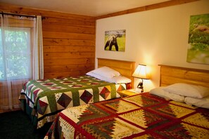 A room with two beds, each with a quilt, a nightstand with a lamp, and a picture on the wall.