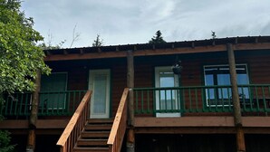 Una cabaña de madera de dos pisos con una escalera de madera que lleva a un balcón.