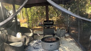 Un espace extérieur aménagé avec des meubles en osier, un barbecue et un tapis à motifs, le tout abrité.