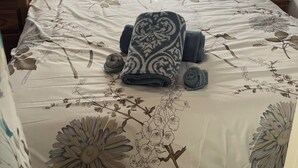 Une chambre à coucher avec un lit, deux oreillers, une couverture et des serviettes enroulées.