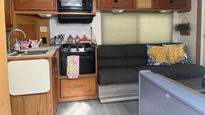 Une cuisine compacte pour camping-car, équipée d’un four à micro-ondes, d’une cuisinière, d’un évier et de meubles de rangement en bois.