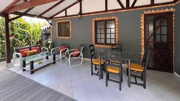 A covered outdoor seating area with a table and chairs, a sofa, and a window with decorative trim. - Charming gîte, in a lush countryside setting yet close to all amenities. (Le Lamentin)