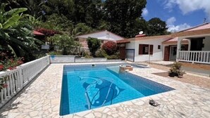 A swimming pool with a stone deck, surrounded by a white fence and lush greenery. - Charming gîte, in a lush countryside setting yet close to all amenities. (Le Lamentin)