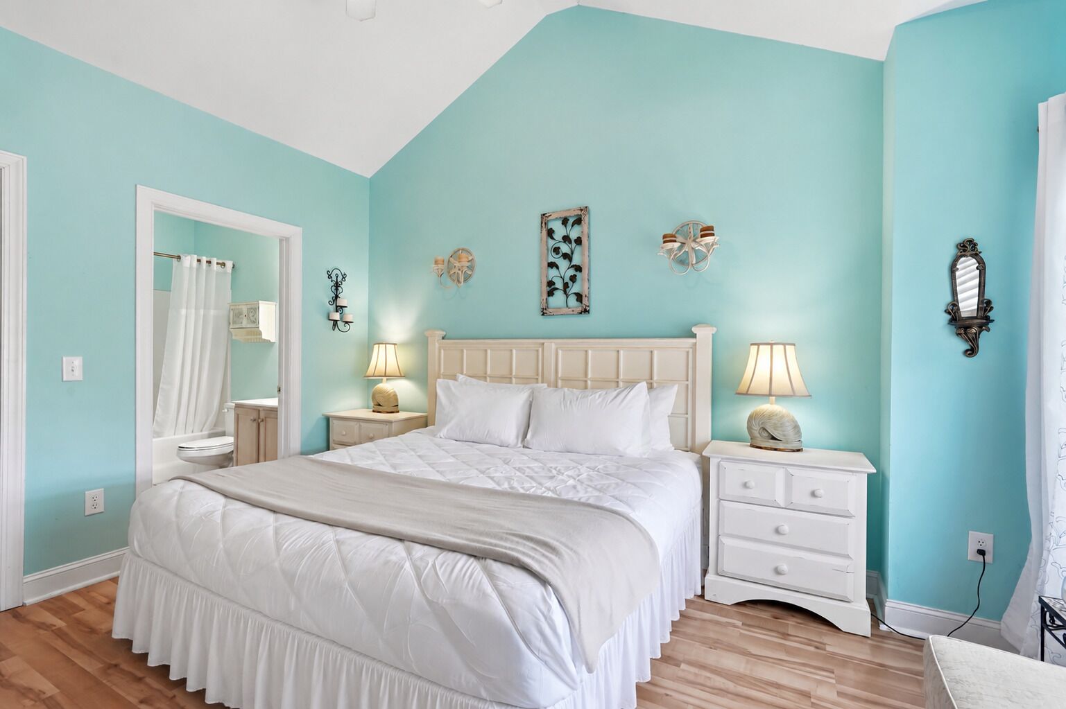 A bedroom with a large bed, two bedside tables, a nightstand, a mirror, and a wall clock.
