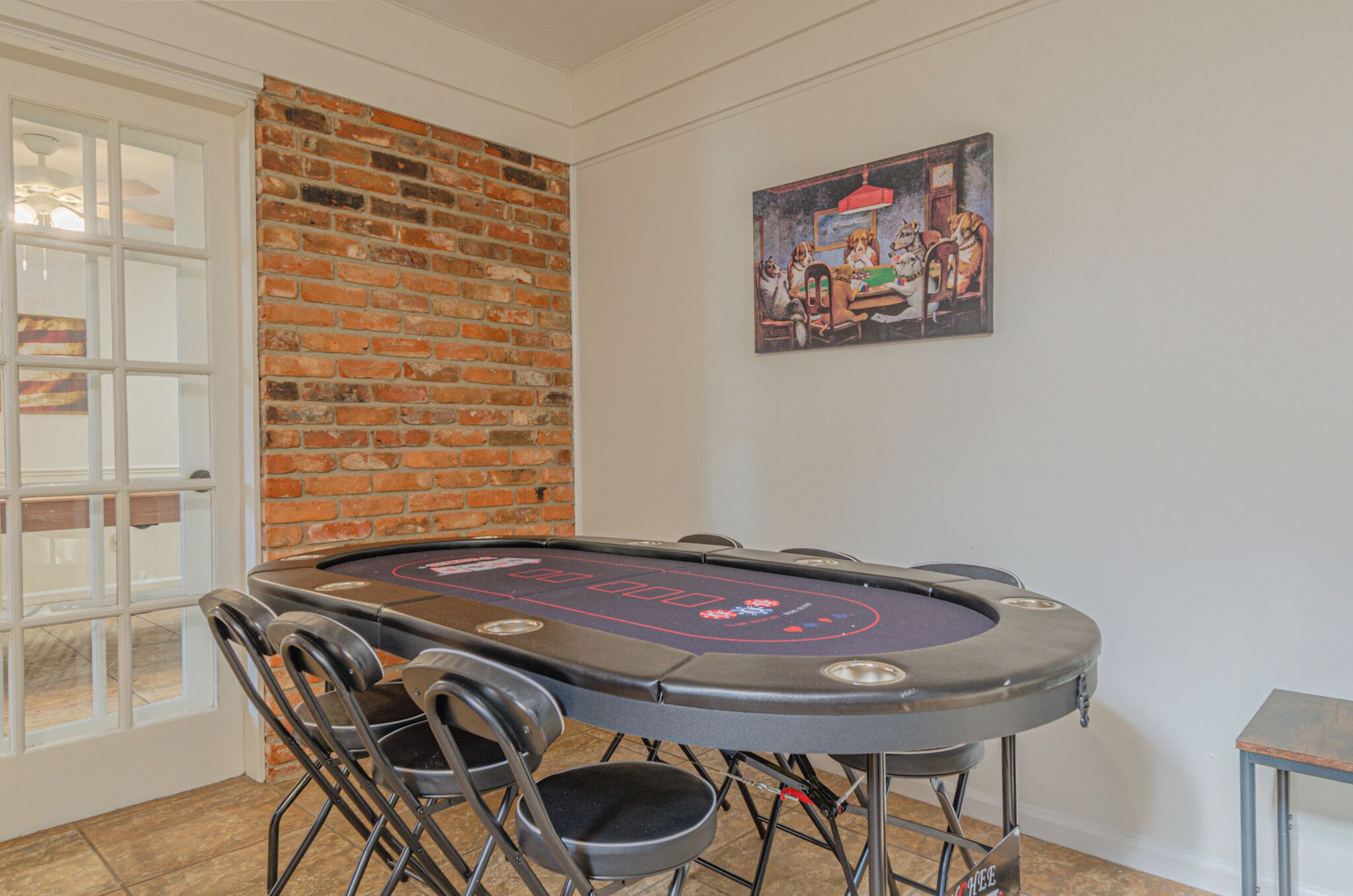 Una mesa de blackjack con sillas, una pared de ladrillo, una puerta y un cuadro en la pared.