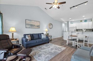 A modern living room with a sofa, chairs, a dining table, and a kitchen area.