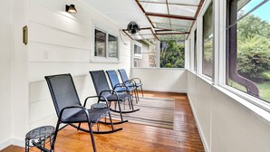 Un solárium con suelo de madera, techo de cristal y una fila de sillas orientadas a un jardín.