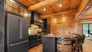 A modern kitchen with a large refrigerator, wooden cabinets, and a bar area with stools. - Buffalo Lodge - Stay for 8 (Branson)