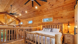 A wooden cabin bedroom with a bed, a nightstand, a lamp, and a ceiling fan. - Buffalo Lodge - Stay for 8 (Branson)