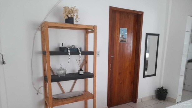Ein Zimmer mit einer Holzhockerreih entlang der Wand, einer Tür mit einem Plakat, einem Spiegel und einem Blumentopf.