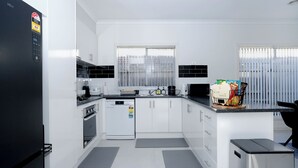 A modern kitchen with white cabinets, a black refrigerator, a dishwasher, and a coffee machine. - Family And Remote Work Friendly-Only 4 Minutes from The Pacific Werribee (Werribee)