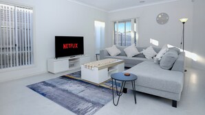 A modern living room with a grey sofa, a coffee table, a TV, and a window with blinds. - Family And Remote Work Friendly-Only 4 Minutes from The Pacific Werribee (Werribee)