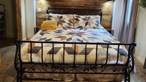 A bedroom with a wooden ceiling, a bed with a patterned quilt, a ceiling fan, and an air conditioning unit. - The Barn in Kirby AR (Amity)