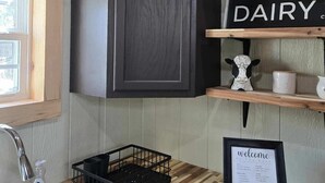 A kitchen with a wooden ceiling, a black cabinet, a 'DAIRY' sign, a welcome sign, and a window with blinds. - The Barn in Kirby AR (Amity)