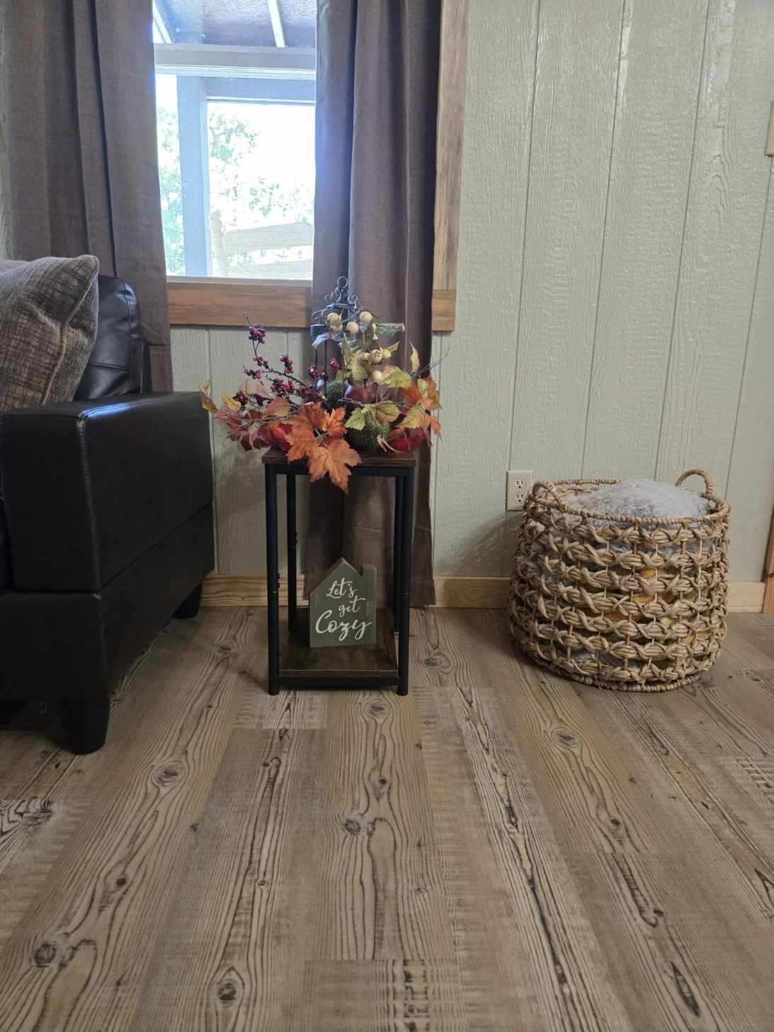 A cozy room with a dark leather sofa, a small wooden table with a house-shaped sign, and a woven pouf.