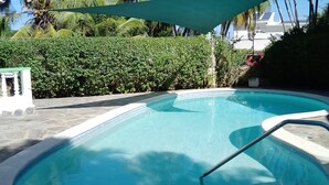 A swimming pool with a stone deck, surrounded by lush greenery and a white fence.