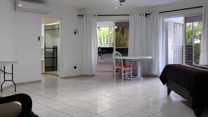 A spacious living room with a ceiling fan, a dining area with a table and chairs, and a bed with a dark cover.