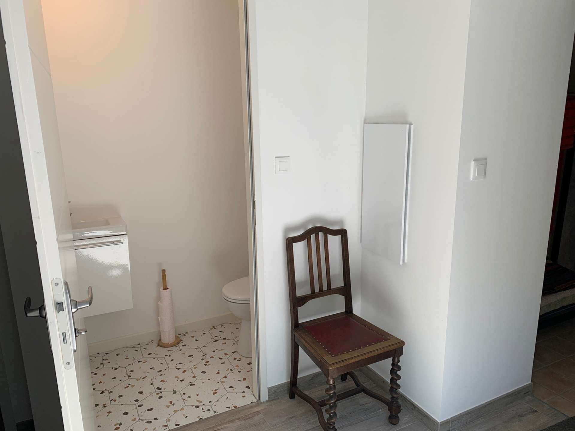 Une salle de bain avec des toilettes, une chaise en bois et un porte-rouleau de papier toilette.
