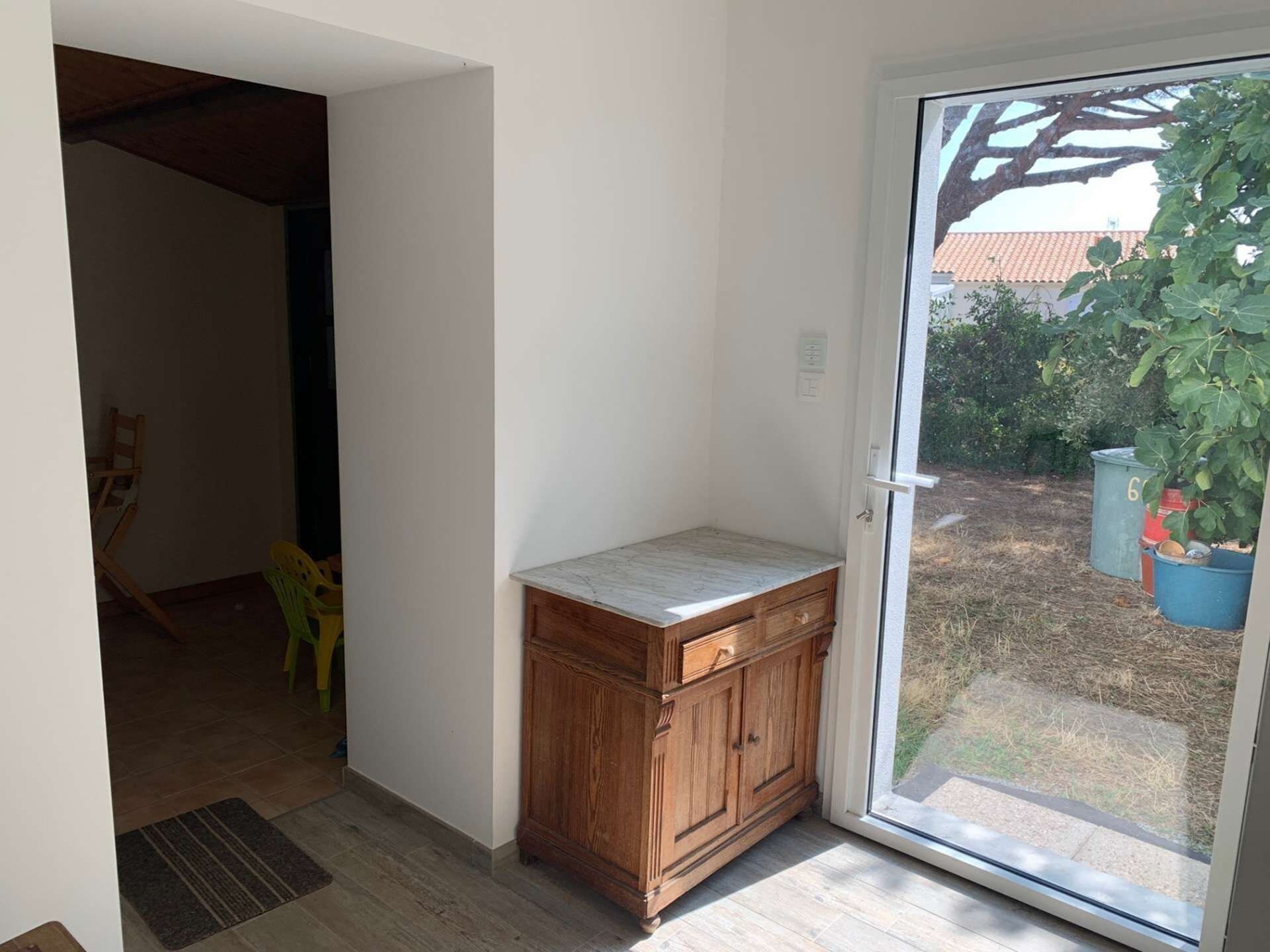 A room with a wooden cabinet, a sliding glass door leading to a garden, and a chair.