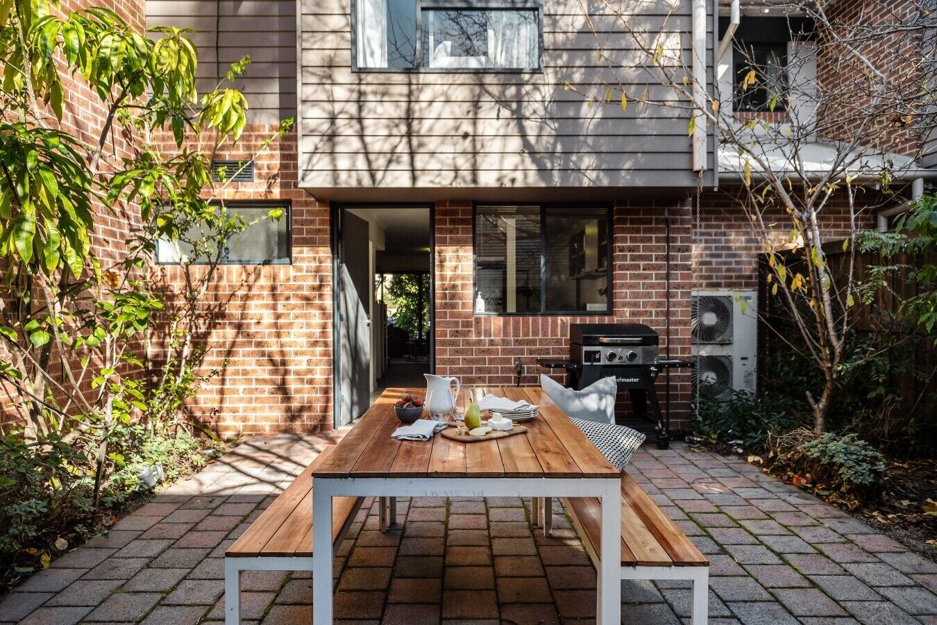 A patio with a wooden table, a grill, and a brick wall.