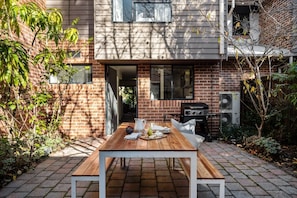 Une terrasse avec une table en bois, un barbecue et un mur en briques.