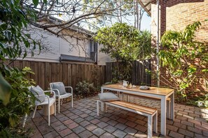 Une terrasse avec une table et des chaises en bois, un sol en briques et une clôture en bois.