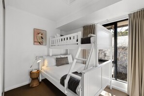Une chambre avec un lit superposé, une fenêtre, une lampe de chevet et un tableau au mur.