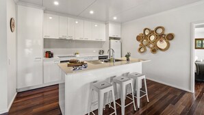 Een moderne keuken met witte kasten, een centraal eiland met krukken en een decoratief houten paneel.