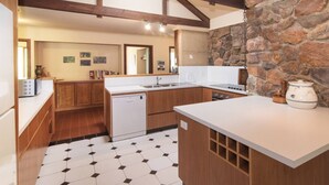 A kitchen with wooden cabinets, a white countertop, a stone wall, and a tiled floor.