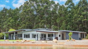 Uma casa moderna de dois andares com uma varanda espaçosa, emoldurada por uma paisagem natural e um corpo d'água.