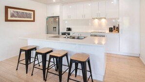 Una cocina moderna con armarios blancos, una isla central con taburetes, electrodomésticos de acero inoxidable y un cuadro en la pared.
