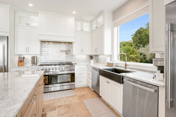 A modern kitchen with white cabinets, stainless steel appliances, a large window, and a view of greenery.