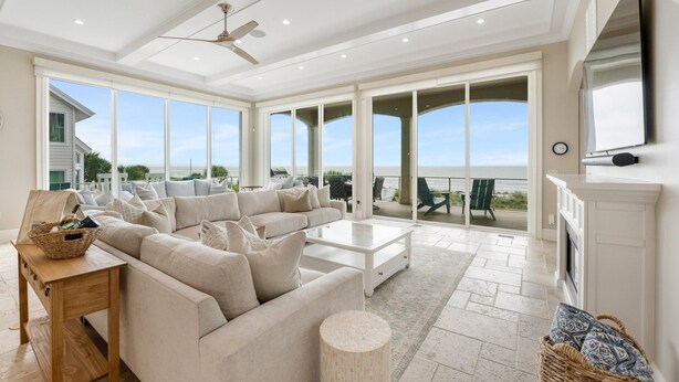 Een ruime woonkamer met een grote beige hoekbank, een witte salontafel en een open haard.