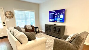 Een woonkamer met een bank, fauteuil en een aan de muur bevestigde televisie.