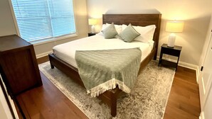 Een slaapkamer met een groot bed, twee nachtkastjes met lampen, een raam met zonwering en een houten vloer.