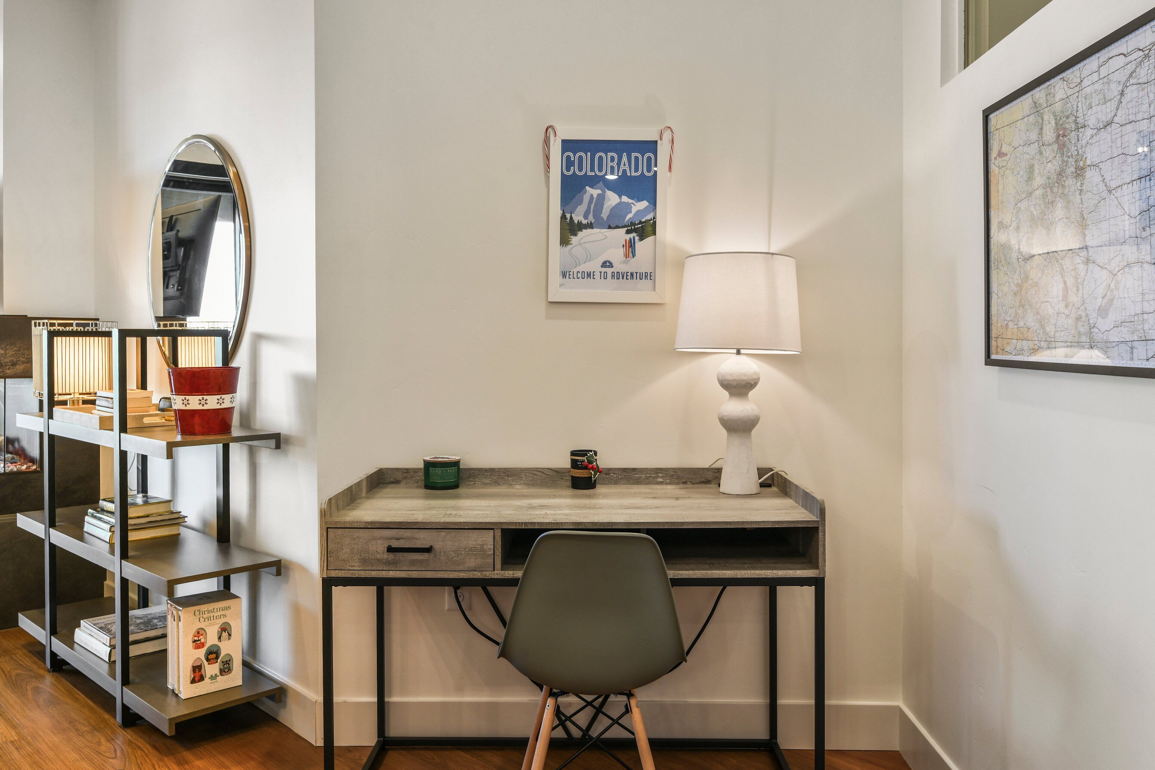 Un espacio de oficina moderno con un escritorio, silla, lámpara, estantería y un cartel de bienvenida enmarcado.