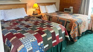 A room with two beds, each covered with a colorful quilt. There is a lamp on one side and a heater on the other. - Hallo Bay Room, Homer Floatplane Lodge (Homer)