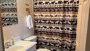 A bathroom with a sink, toilet, and a shower curtain with a wildlife pattern. - Hallo Bay Room, Homer Floatplane Lodge (Homer)