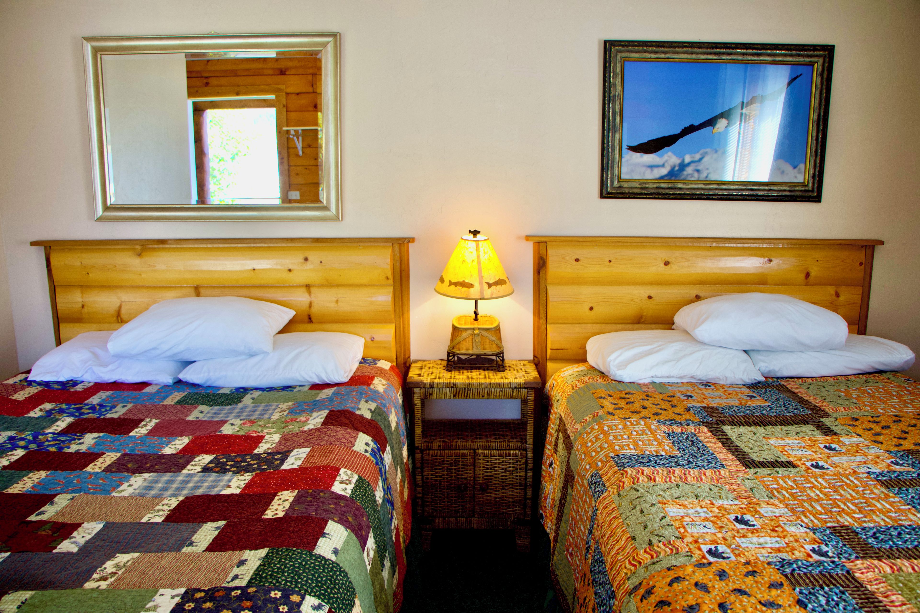 Two double beds with wooden headboards, a nightstand with a lamp, and a mirror on the wall.