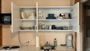 A kitchen with white cabinets, a stove, a sink, and various kitchen items like plates and glasses. - Hallo Bay Room, Homer Floatplane Lodge (Homer)