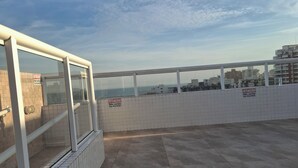 A rooftop terrace with a view of the city skyline, tiled walls, and a metal railing. - 2 bedrooms, 1 suite, 2 bathrooms, balcony with sea view, wifi, hammock, cozy (Cidade Ocian Praia Grande)