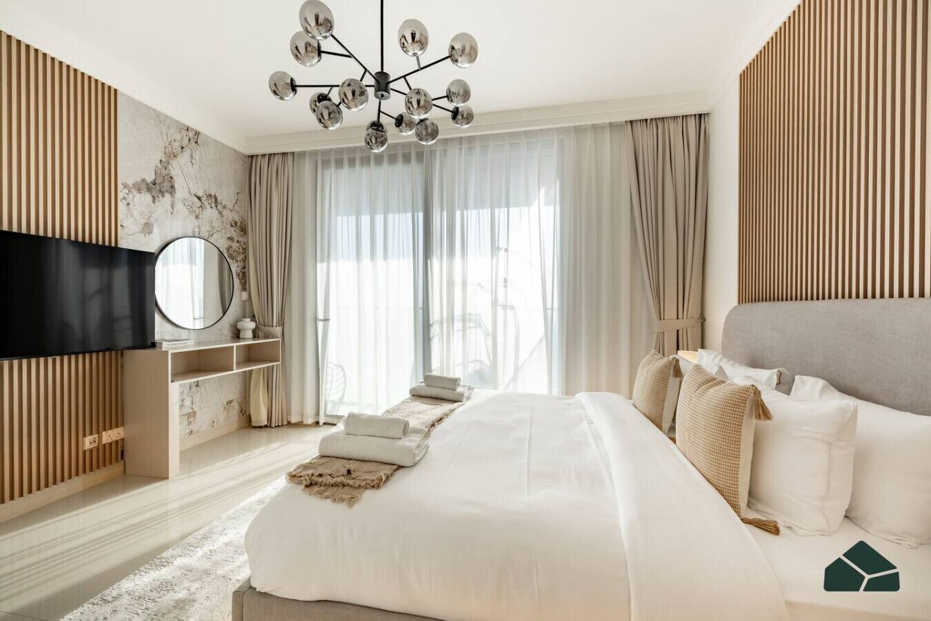 Une chambre à coucher moderne avec un grand lit, un téléviseur fixé au mur et un lustre original.