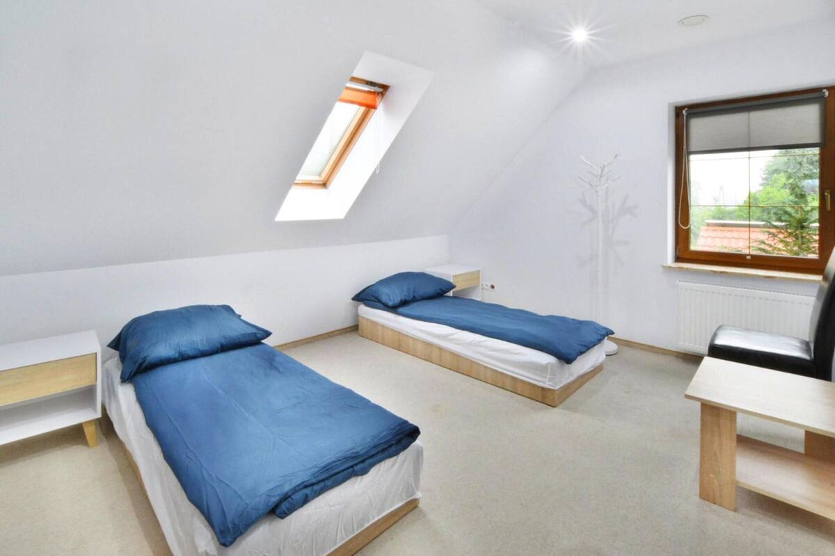 A dormitory room with two single beds, a small table, a window with a view, and a radiator.